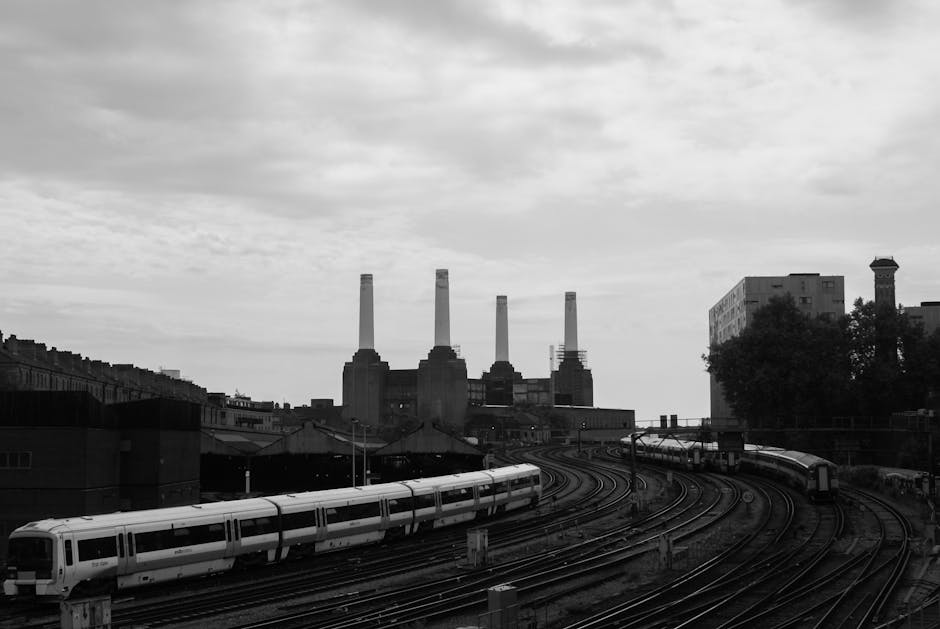 A high-rise building with a brick base and three tall, cream-colored industrial chimneys extending upward against a clear blue sky. The tallest chimney is on the right side of the image, with a smalle